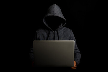 Man without a face in a hood holds a laptop on a dark background. Concept of cyber rogue, hacker....
