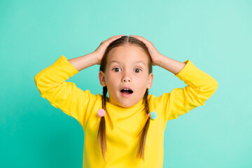 Photo of astonished surprised little schoolgirl unexpected news hands head isolated on vivid teal...