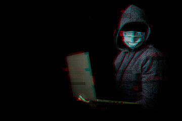 Man in a mask without a face and a hood holds a laptop in his hands on a dark background. Concept of cyber rogue, hacker. Banner. Added glitch effect