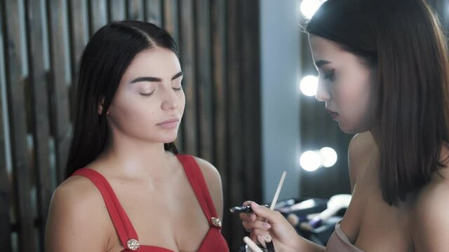 Woman makeup artist applies makeup to cute young caucasian model 