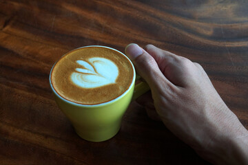 Drink scene of Hot Latt Coffee in yellow Cup on Brown wood Table at Coffee Cafe in Danang Vietnam