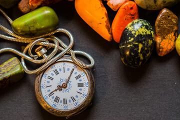 An old watch with a chain among colorful pebbles.