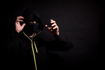 Masked thief is trying to scare you with raised arms isolated on black background