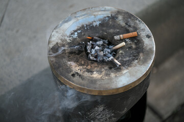 Cigarette butts thrown into a metal street ashtray burning and causing an open flame