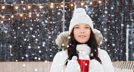 christmas, winter holidays and leisure concept - happy young woman with tea cup over ice skating rink on background