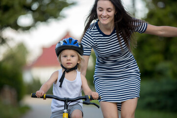 Obraz premium Young mother, helping her son to learn how to ride a bike, holding him and teaching him