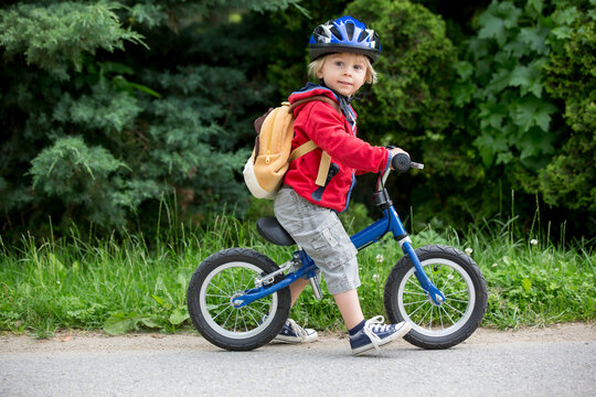 Cute toddler boy with blue helmet, riding balance bike on the street