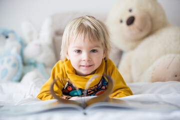 Beautiful child, toddler boy, reading book and playing with it, creative knowledge shot with book