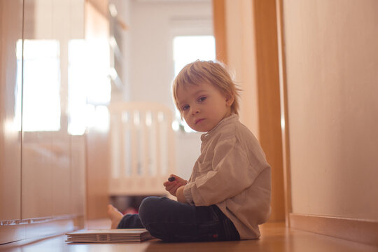 Beautiful toddler blond boy, lying on the floor at home in the hall, reading book
