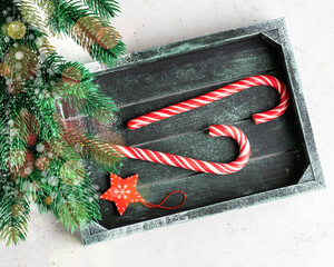 Festive composition. Candy canes, red decorations in wooden box on white stone background. Christmas, winter, new year concept