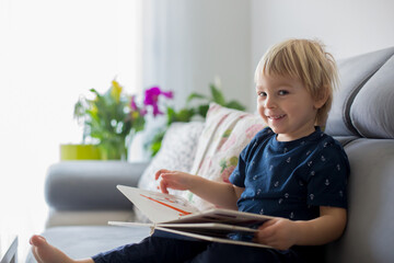 Young woman, mother with three kids, reading a book at home, hugging and laughing