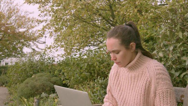 Female working on a laptop in a park stressed