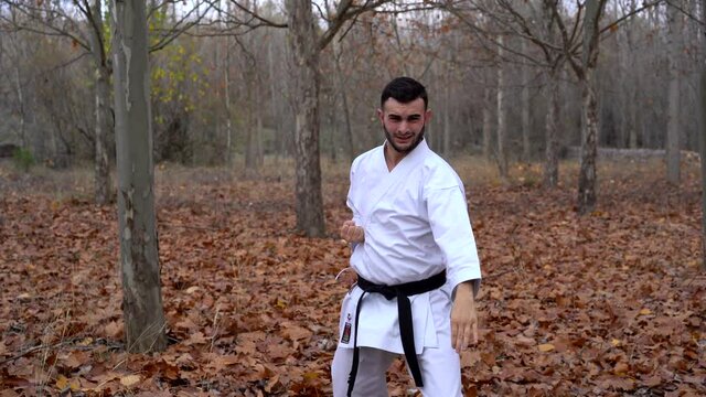 Black belt karate fighter concentrated man practicing martial arts technique kicking and punching outdoors in an autumn landscape. Traditional karate wado Ryu