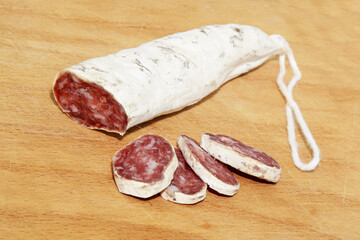 Close-up Italian and Catalonia Fuet cured pork sausage with slices on wooden table. Sausage from minced pork seasoned with pepper - traditional meat product of Western Europe. Selective focus