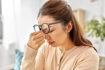 fatigue, stress, vision and people concept - tired asian woman with glasses rubbing nose bridge at home