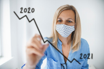 Business woman with face mask drawing falling graph for 2021