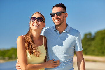 leisure, relationships and people concept - happy couple in sunglasses hugging on summer beach