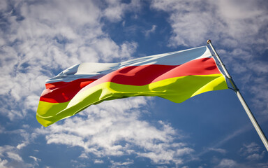 Beautiful national state flag of North Ossetia fluttering at sky background. Low angle close-up North Ossetia