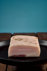 Lardo Speck auf schwarzem Teller auf Holztisch mit blauem Hintergrund
