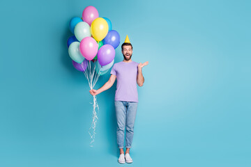 Full length body size photo of excited birthday man pile of balloons wearing yellow headwear smiling isolated on vivid blue color background