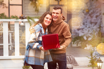 Couple hugging and celebrating New year outdoors. They holding red box with Valentine's gift. They laughing and enjoying