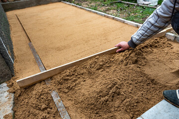 Worker screeding sand bedding to level for laying paving slabs.