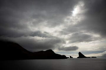 Fototapeta na wymiar Tindholmur boulder peak against dark cloudy sky, backlit
