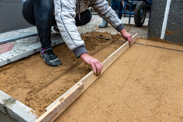 Worker screeding sand bedding to level for laying paving slabs.