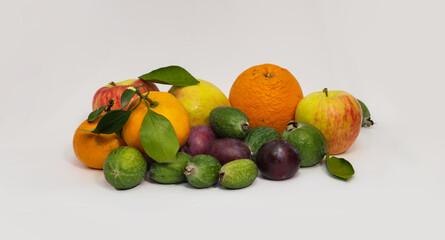 Still life of fruits: tangerines with leaves, plums, feijoa, apples, oranges on a light background.