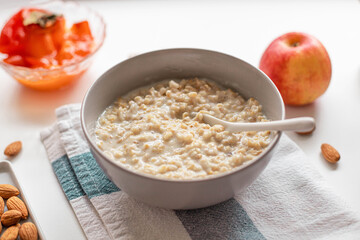 Homemade oatmeal porridge with nut almonds in a bowl, ceramic spoon, red apple on white background. Health breakfast food concept