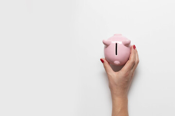 Woman's hand with red manicure holds money piggy bank on white background. Flat lay, top view,...