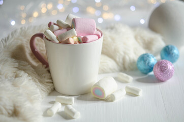 Obraz na płótnie Canvas Cup with marshmallows and colored balls on a white table.