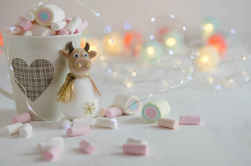 Cup with a pattern full of marshmallows and a toy bull on a blurred background