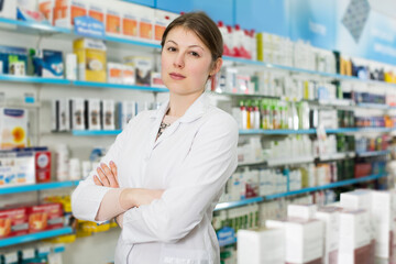 Confident young woman pharmacist standing with arms crossed in interior of pharmacy
