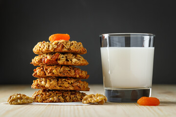 Sweet oatmeal cookies with dried apricots, nuts and a glass of milk on a wooden table.