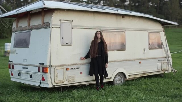 A beautiful young woman in black clothes walks in nature and poses against the background of a travel trailer. Slow motion