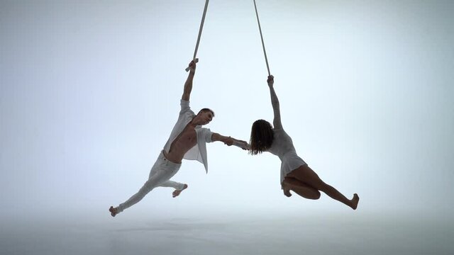 Aerial straps duo wearing white costume on white background doing performance in slow motion. Concept of desire, attraction and relationship
