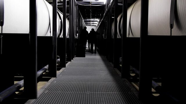 Rear view of three men walking along water treatment tanks at the power plant. Media. Corridor with huge reservoir tanks for water purification, ecology concept.