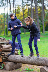 teens relaxing outdoor in autumn city park, happy people together, boy and girl, they standing on a log, playing, talking and smiling, beautiful nature