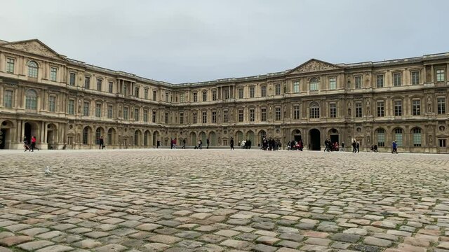 Time lapse footage of people walking at world's largest art museum and a historic monument called "Louvre" in Paris. it's a cloudy winter day.