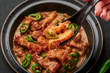 Bicol Express Stew in black bowl on dark slate table top. Filipino cuisine spicy pork belly coconut milk curry. Asian food.