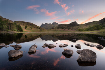 Perfect reflections of a beautiful sunrise with scattered rocks in foreground at Blea Tarn in the...