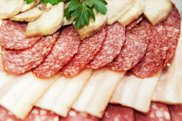 Sausage and bacon dish, garnished with herbs. Sliced meat products lie on a plate in rows. Close-up