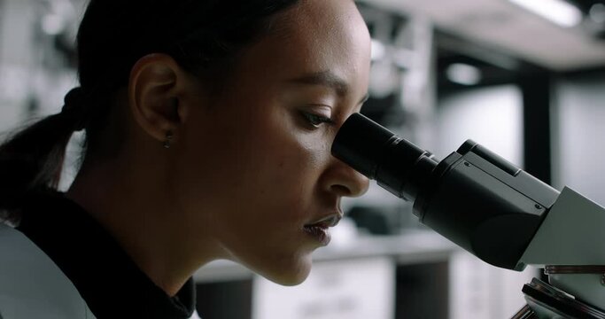 CU Portrait of Middle Eastern female scientist looking through a microscope in a laboratory. Young scientist doing some research