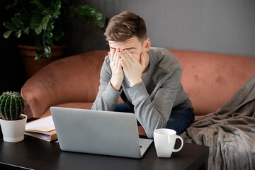 Feeling tired. Frustrated young  man looking exhausted and covering his face with hands while...