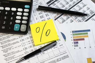 on documents with numbers and a chart next to a black calculator is a sheet for notes with a percentage drawn on it