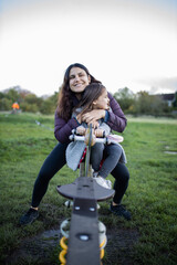 Joyful mother and little daughter smiling while playing on a seesaw