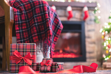 Fototapeta premium Woman legs in a winter socks covered plaid sitting and relaxation on armchair near fireplace and christmas tree pakking gift boxes for family. Bottom view.