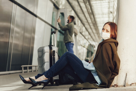 Young woman in medical mask sits near luggage in airport. Tortured by the flight, the woman dozes off before the next flight. Travel and coronavirus concept