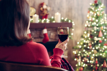 Back view of woman drinking wine from glass covered plaid sitting and relaxation on armchair near...